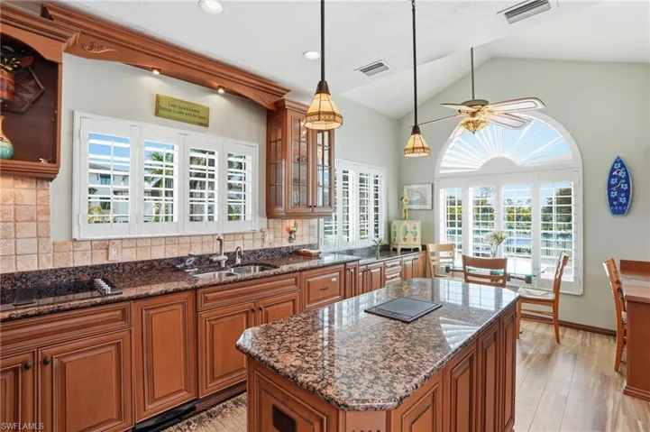 Kitchen featuring wood finish cabinetry, tasteful backsplash, dark stone countertops, lofted ceiling, and glass insert cabinets