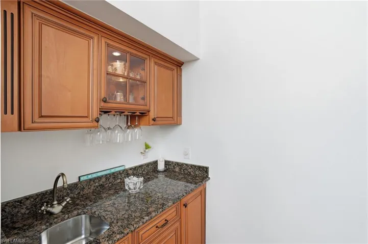 Indoor wet bar featuring dark stone countertops, glass fronted cabinets, and wood finish cabinetry