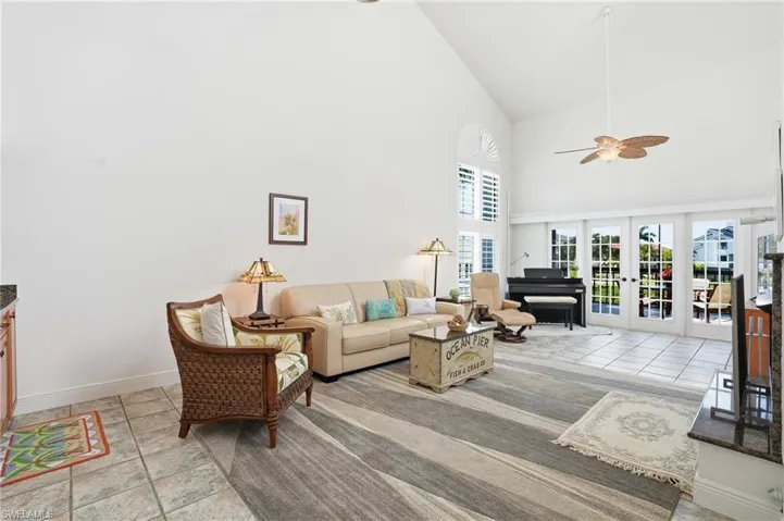 Living room with vaulted ceiling, light tile patterned flooring, ceiling fan, and french doors