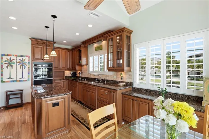 Kitchen featuring wood finish cabinets, a center island, glass insert cabinets, dark stone countertops, and decorative light fixtures