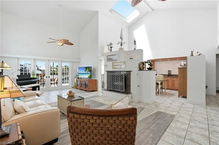 Living area featuring a ceiling fan, a skylight, vaulted ceiling, light tile patterned flooring, and a high end fireplace