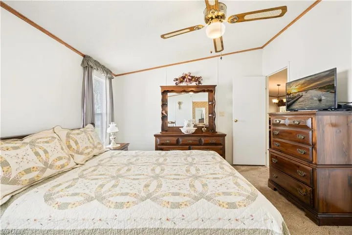 Carpeted bedroom with ornamental molding, vaulted ceiling, and a ceiling fan