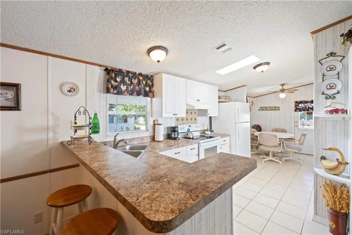 Kitchen with white electric range oven, a peninsula, a ceiling fan, a kitchen breakfast bar, and white cabinetry