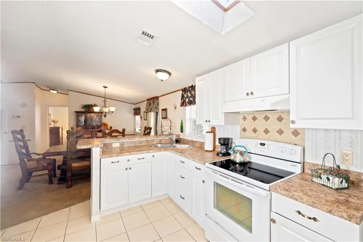 Kitchen with white electric stove, a peninsula, under cabinet range hood, a skylight, and light tile patterned flooring