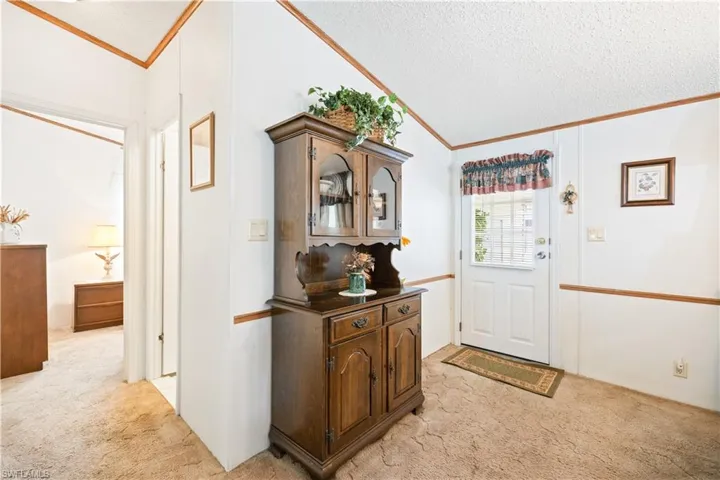 Foyer entrance featuring light carpet, crown molding, vaulted ceiling, and a textured ceiling