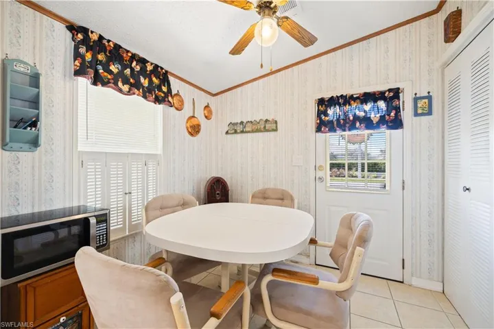 Dining area with crown molding, wallpapered walls, ceiling fan, and light tile patterned floors
