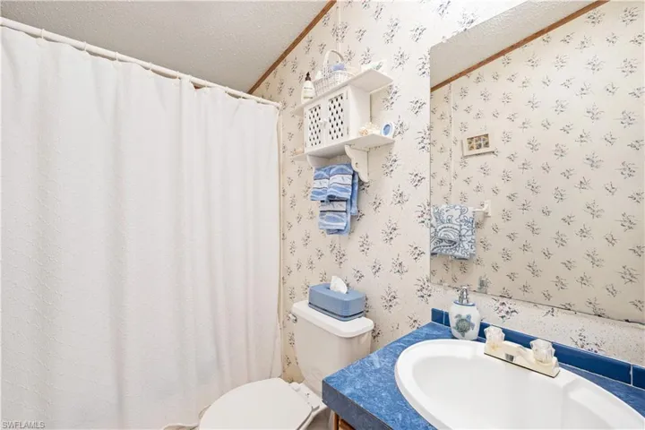 Bathroom with wallpapered walls, a textured ceiling, vanity, a shower with shower curtain, and crown molding