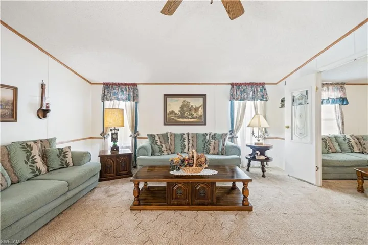 Living room featuring healthy amount of natural light, light carpet, a textured ceiling, ornamental molding, and ceiling fan