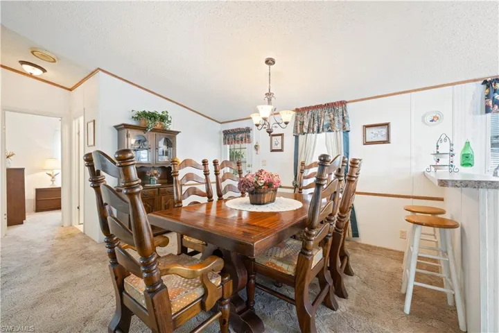 Dining area featuring light colored carpet, a chandelier, crown molding, and a textured ceiling
