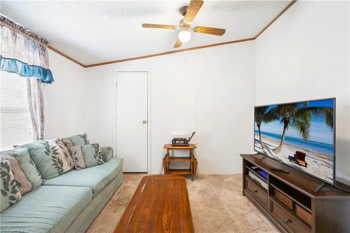 Living area with light carpet, crown molding, lofted ceiling, a ceiling fan, and a textured ceiling