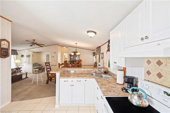 Kitchen featuring stove, a peninsula, lofted ceiling, under cabinet range hood, and light countertops