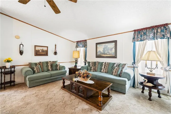 Living room with crown molding, carpet flooring, vaulted ceiling, a ceiling fan, and a textured ceiling