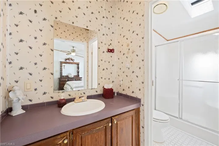 Ensuite bathroom with wallpapered walls, a skylight, a shower with door, and vanity