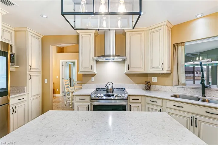 Kitchen featuring light stone  - Virtually Edited Imagecountertops, pendant lighting, cream cabinets, stone tile floors, and lofted ceiling