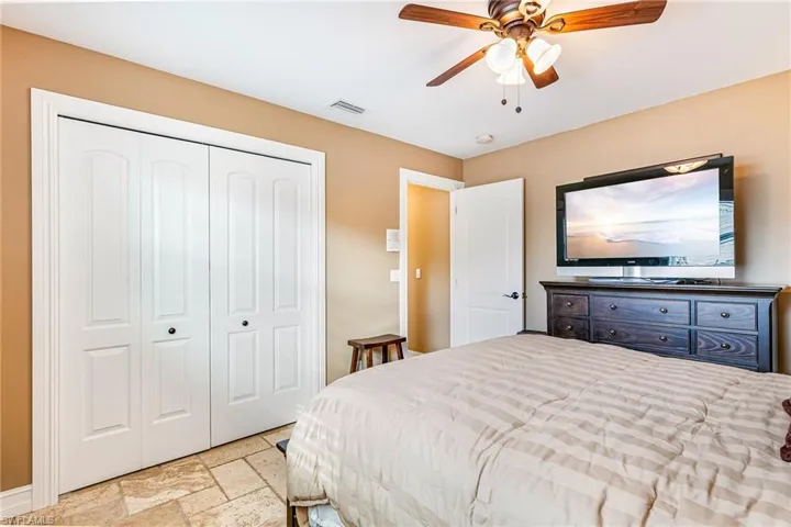 Bedroom featuring a closet, stone tile floors, and a ceiling fan - Virtually Edited Image