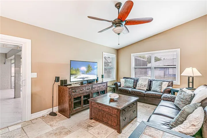 Living area featuring vaulted ceiling, ceiling fan, plenty of natural light, and stone tile flooring - Virtually Edited Image
