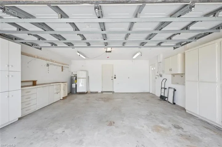 Expansive garage space featuring a concrete floor, extensive built-in white cabinetry, a built-in workbench, and overhead lighting