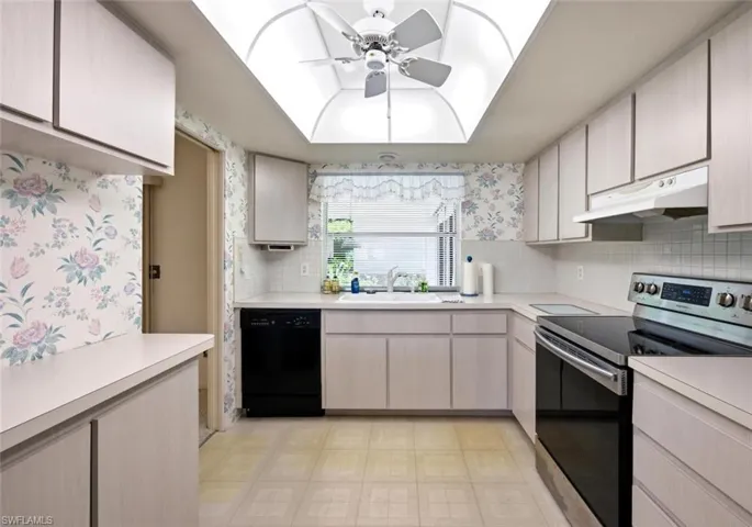 Bright kitchen featuring a skylight with a ceiling fan, white cabinetry, white countertops, and a full suite of appliances including a black dishwasher and a stainless steel range with a black cooktop