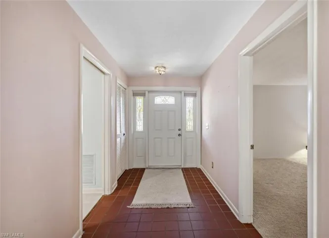 Entryway featuring terracotta-style tile flooring, a paneled front door with decorative glass inserts, and sidelight windows
