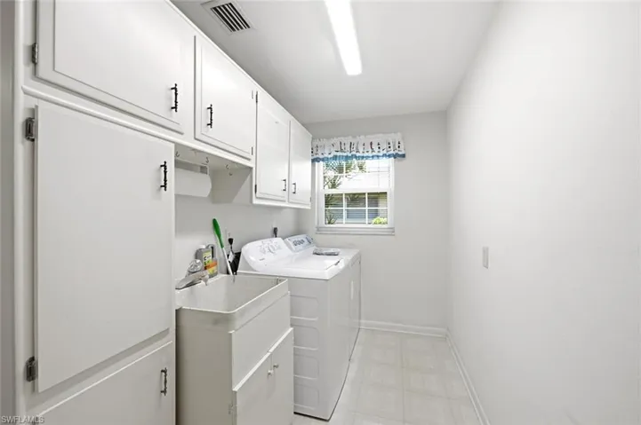 Dedicated laundry space featuring extensive white cabinetry, a utility sink, and ample overhead storage