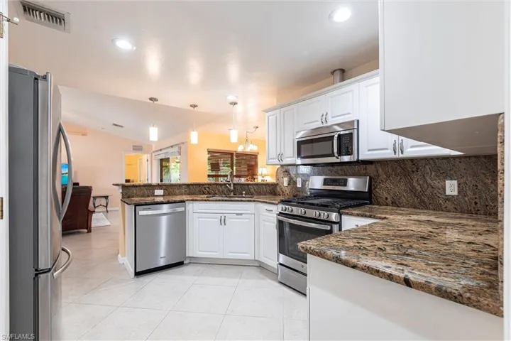 Kitchen with a peninsula, appliances with stainless steel finishes, a sink, and lofted ceiling