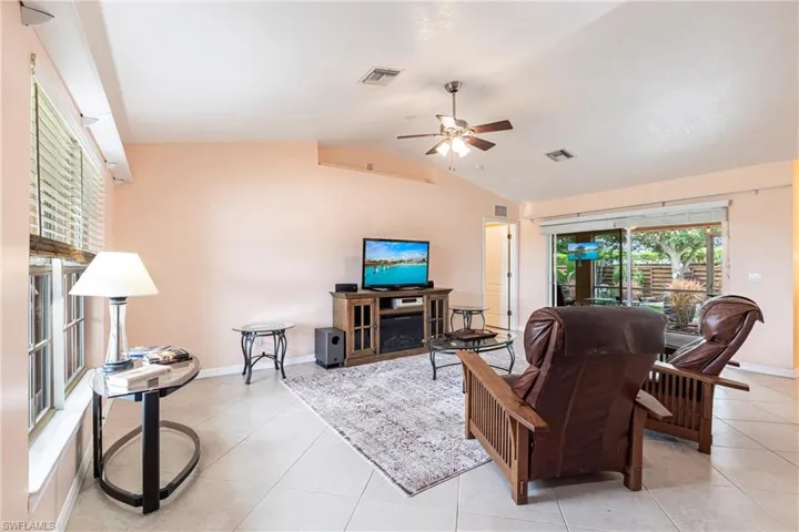 Living room featuring ceiling fan, light tile  and vaulted ceiling