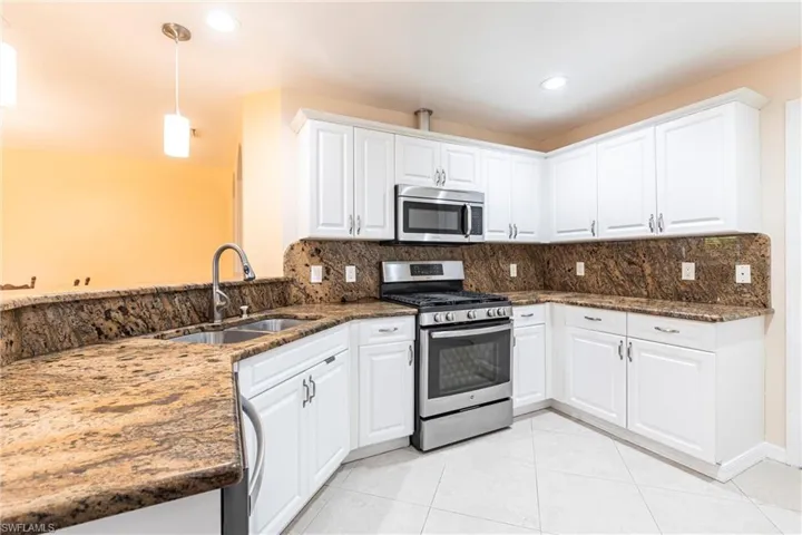 Kitchen featuring white cabinetry, backsplash, granite counters, stainless steel appliances, and a sink