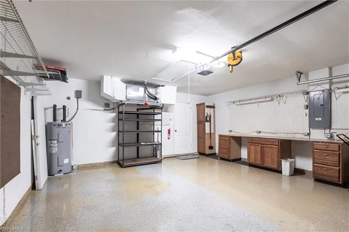 Garage with electric panel, water heater, baseboards, and storage cabinets opener