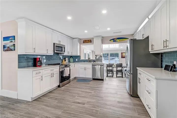 Kitchen with stainless steel appliances, white cabinetry, light stone countertops, wood finish floors, and recessed lighting