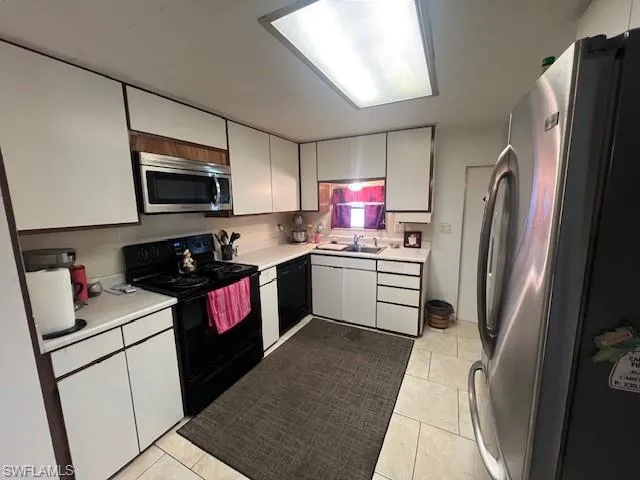 Kitchen with black appliances, light countertops, and light tile patterned floors