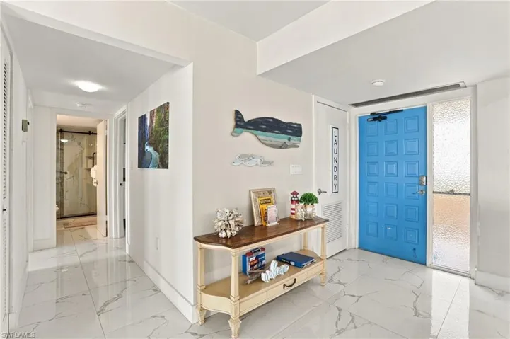 White tile flooring, a blue paneled entry door, a sidelight with textured glass, and a hallway leading to a bathroom with a glass-enclosed shower - Virtually Edited Image