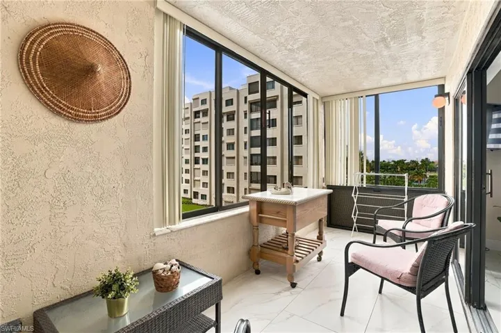 Enclosed balcony featuring large windows, vertical blinds, an overhead wall sconce, and white tile flooring - Virtually Edited Image