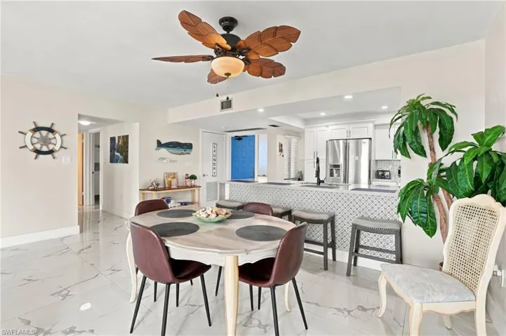 White tile flooring throughout, kitchen with white cabinetry, stainless steel appliances, breakfast bar with patterned tile facade, and recessed lighting - Virtually Edited Image