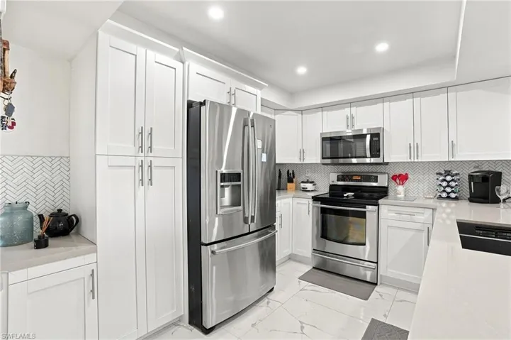 White shaker-style cabinetry, stainless steel appliances, herringbone tile backsplash, recessed lighting, and light-colored countertops - Virtually Edited Image