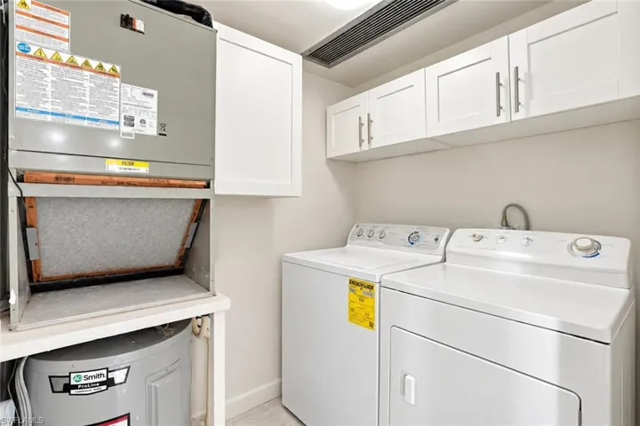 Utility room featuring white cabinetry with brushed nickel pulls, a water heater, and an HVAC unit - Virtually Edited Image