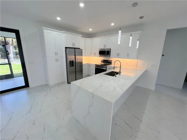 Kitchen with an upgraded waterfall counter, stainless steel appliances, white cabinets, light stone countertops, and hanging light fixtures