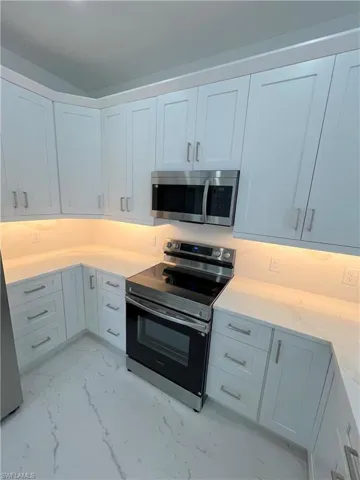 Kitchen featuring stainless steel appliances, white cabinetry, and light stone countertops