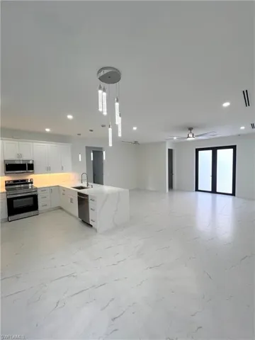 Kitchen with open floor plan, white cabinetry, a peninsula, stainless steel appliances, and hanging light fixtures
