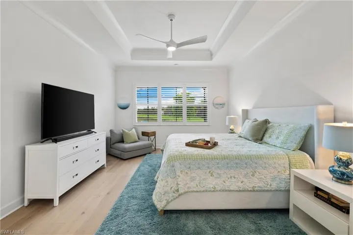 Spacious room featuring wood flooring, a tray ceiling with a modern ceiling fan, and white window shutters