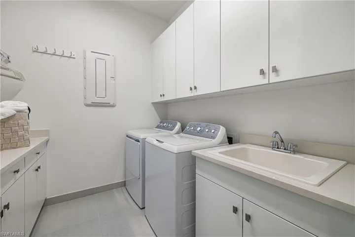 Dedicated utility space featuring a built-in sink, ample white cabinetry for storage, light-toned countertops, and neutral floor tiling