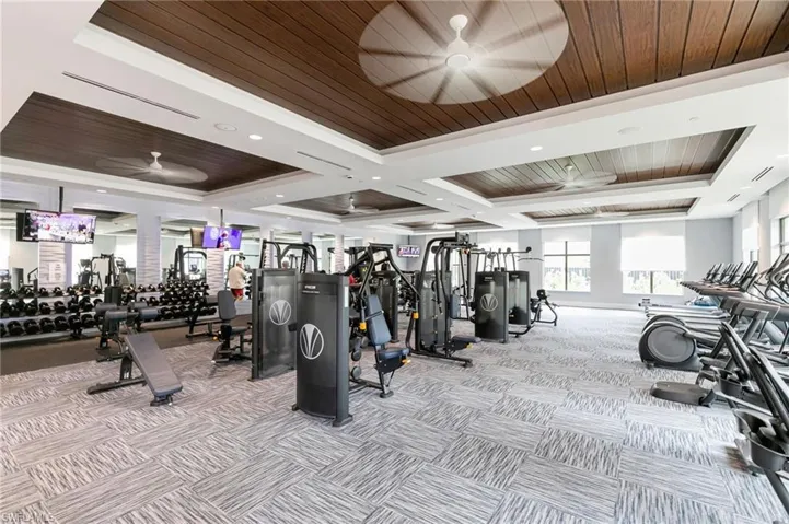 Spacious fitness center featuring a patterned carpet, recessed lighting, and a tray ceiling with wood-finish panels