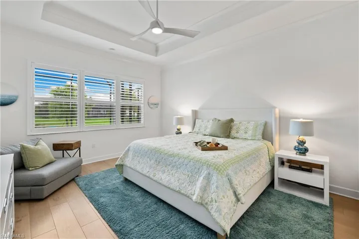 Spacious room featuring wood flooring, a tray ceiling with a ceiling fan, and large windows with plantation shutters