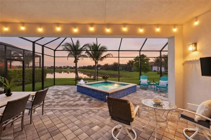 Screened lanai featuring a built-in spa with blue tile surround, paver flooring, overhead string lighting, and a water view.