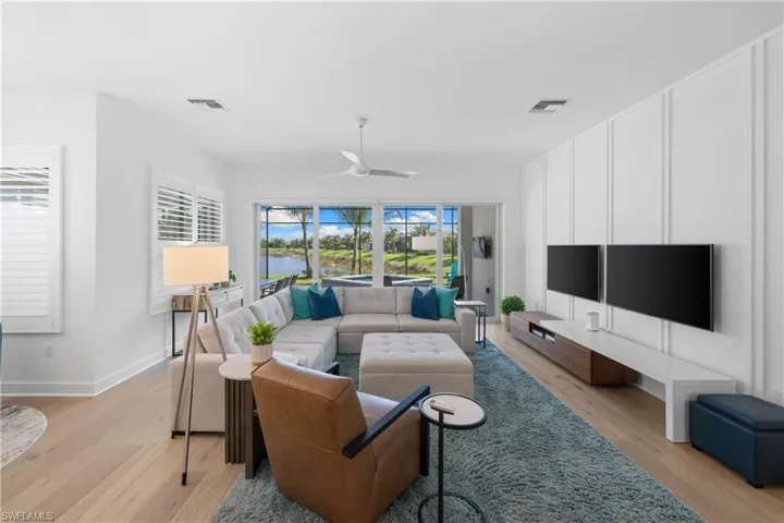 Spacious living area featuring expansive glass sliding doors opening to a screened patio, wood-finish flooring, and a decorative accent wall