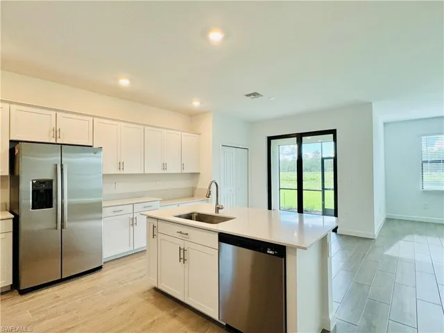 Kitchen with stainless steel appliances, white cabinetry, an island with sink, wood tiled floors, and light stone countertops