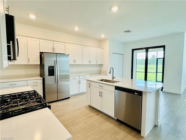 Kitchen with black appliances, white cabinets, a kitchen island with sink, light stone countertops, and recessed lighting