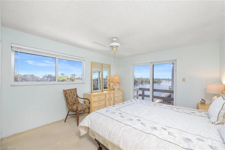 Bedroom featuring a water view, access to exterior, light carpet, baseboards, and ceiling fan