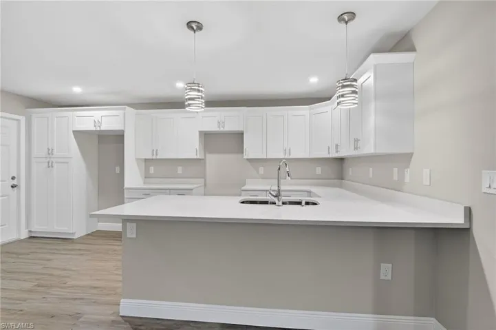 Kitchen featuring pendant lighting, white cabinets, a peninsula, light wood-style flooring, and light stone counters