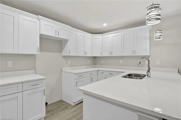 Kitchen featuring white cabinets, hanging light fixtures, light stone counters, light wood-style flooring, and a peninsula