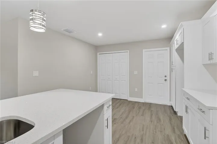Kitchen featuring white cabinets, pendant lighting, light stone counters, and light wood finished floors
